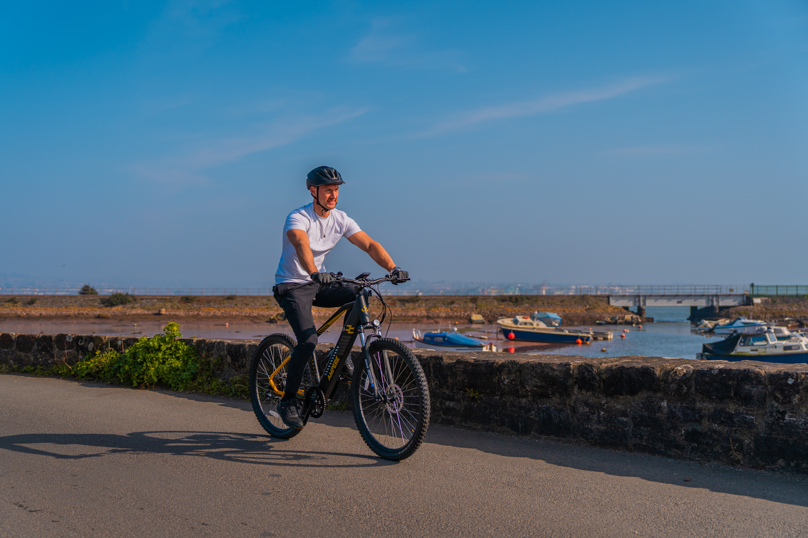 Man riding an Ampere electric bike on the Road next to water with Boats and